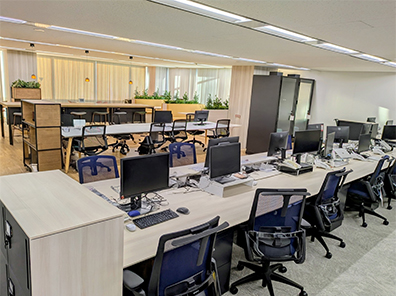 オフィス内の様子。個人デスクにはデスクトップPCと電話機があり、奥にカフェエリアが併設されている。