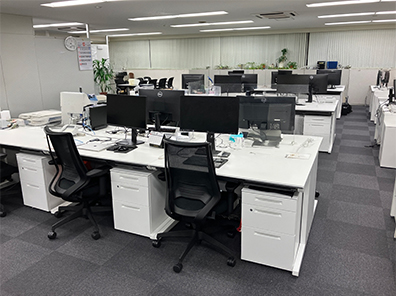 オフィス内の様子。個人デスクにはデスクトップPCと電話機があり、モノトーン基調のオフィス。