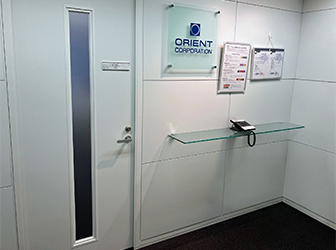 オフィス受付。壁には企業ロゴやISO14001の登録書、SDGs宣言書が掲示されている。ガラス張りの机の上には受付電話機が置かれている。